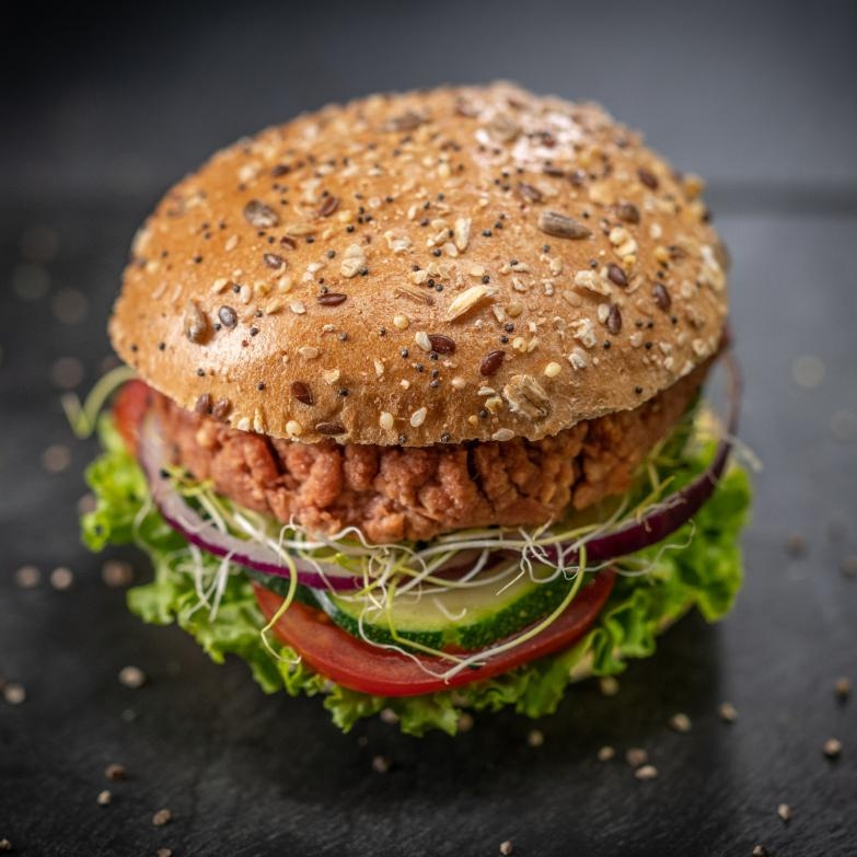 Burger végétal avec salade, des trasnches de concombre, de tomate, des oignons et un steak végétal, posé sur une ardoise