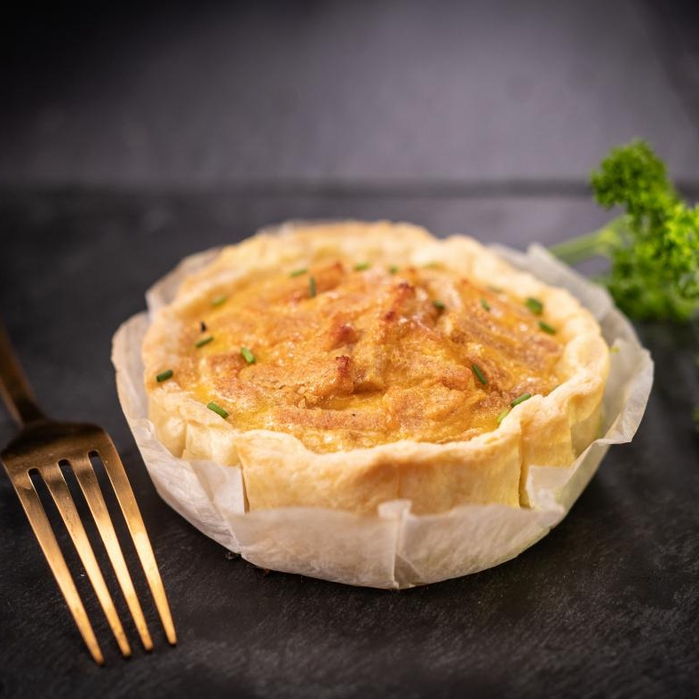 Quiche lorraine végetale, avec une fourchette dorée et une branche de persil, posée sur une ardoise