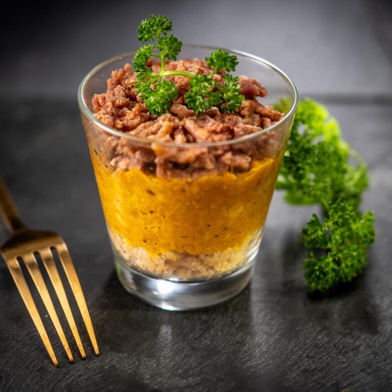 Verrine, facon crumble, viande végétale, avec une fourchette dorée et une branche de persil, sur une ardoise