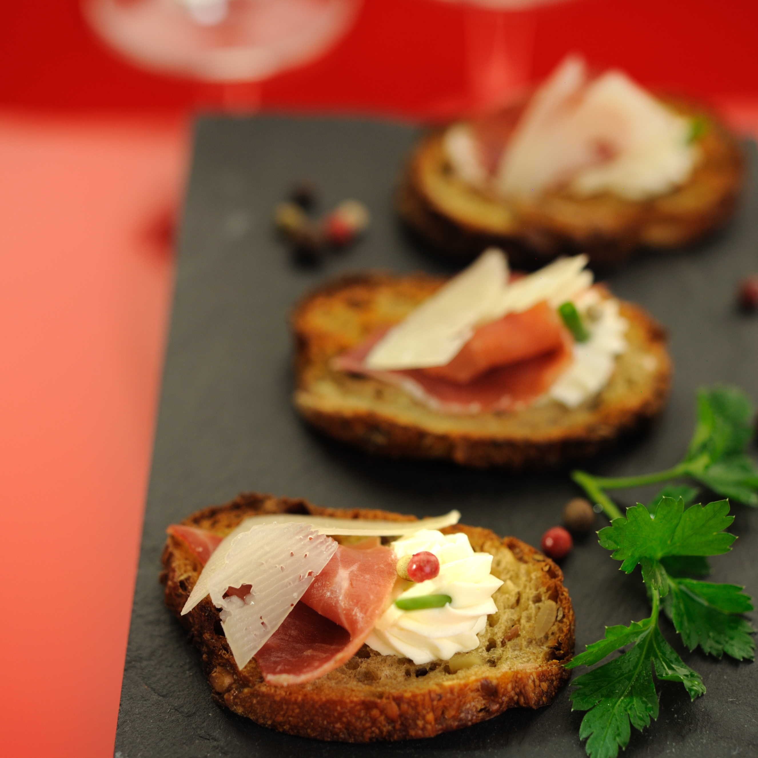 Toast apéritif jambon et parmesan, sur une ardoise, avec des grains de poivre et des feuilles de persil, vue de dessus