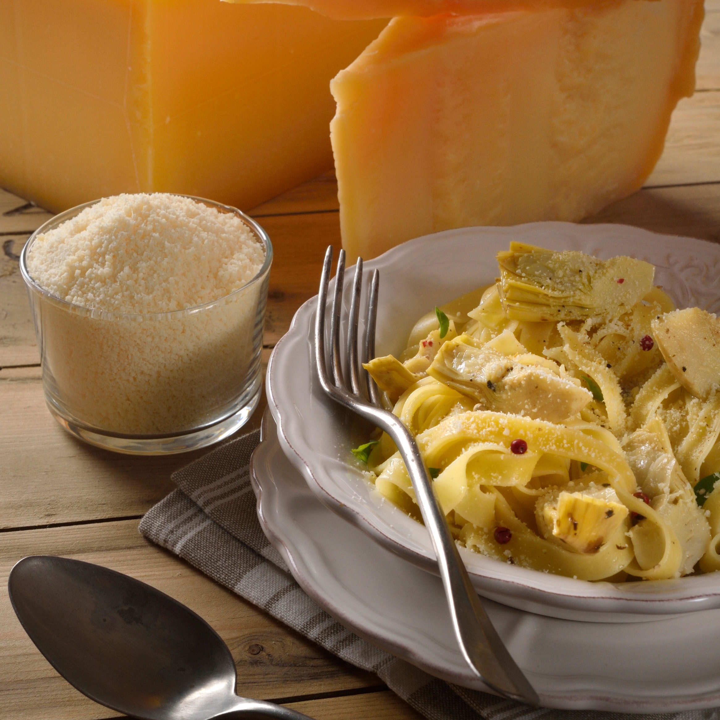 Tome de parmesan, parmesan rapé et assiette de tagliatelles au premier plan